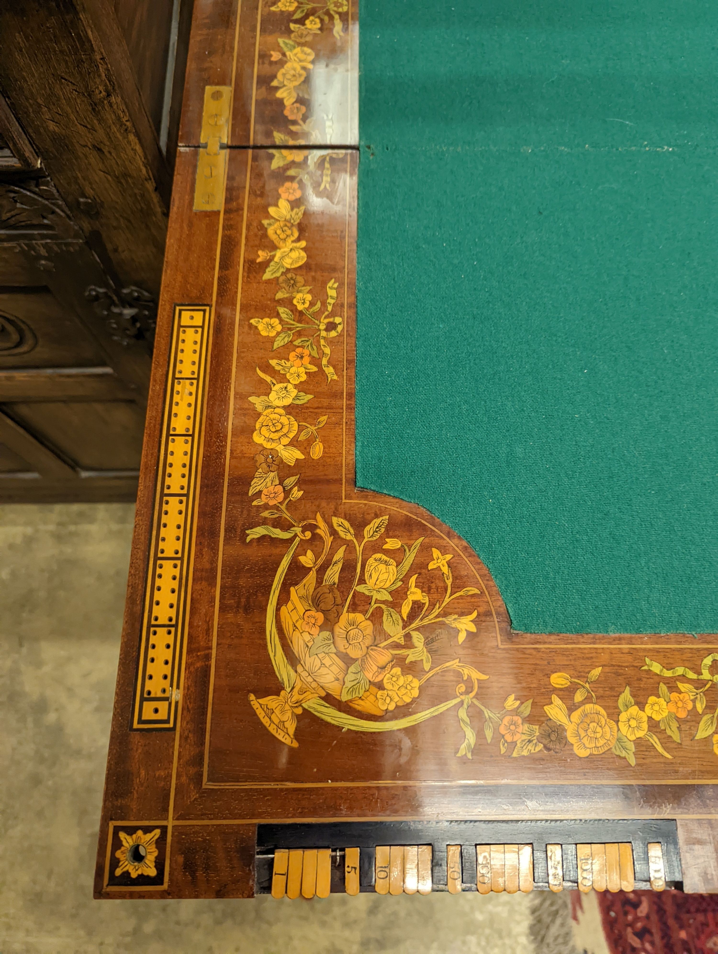 An Edwardian marquetry inlaid mahogany folding games table by W. Thornhill & Co., London, the interior baize lined surface with cribbage board and hinged markers, width 76cm, height 76cm